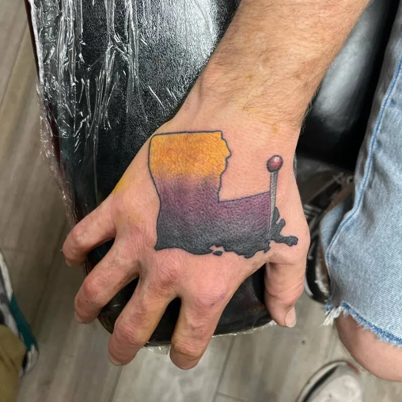 Watercolor tattoo of the state silhouette of Louisiana in an orange and purple gradient with a red map pin, on the hand, by Franky Sharpz at Wailana Tattoo, Waikiki, Hawaii.