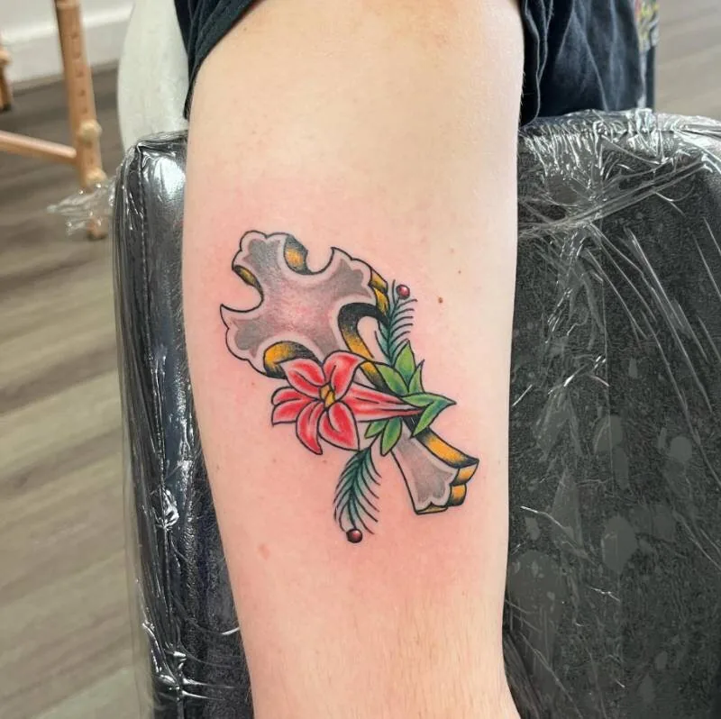 American Traditional color tattoo of an ornate black and yellow cross with a coral tiger lily and palm fronds, on the upper arm, by Franky Sharpz at Wailana Tattoo, Waikiki, Hawaii.